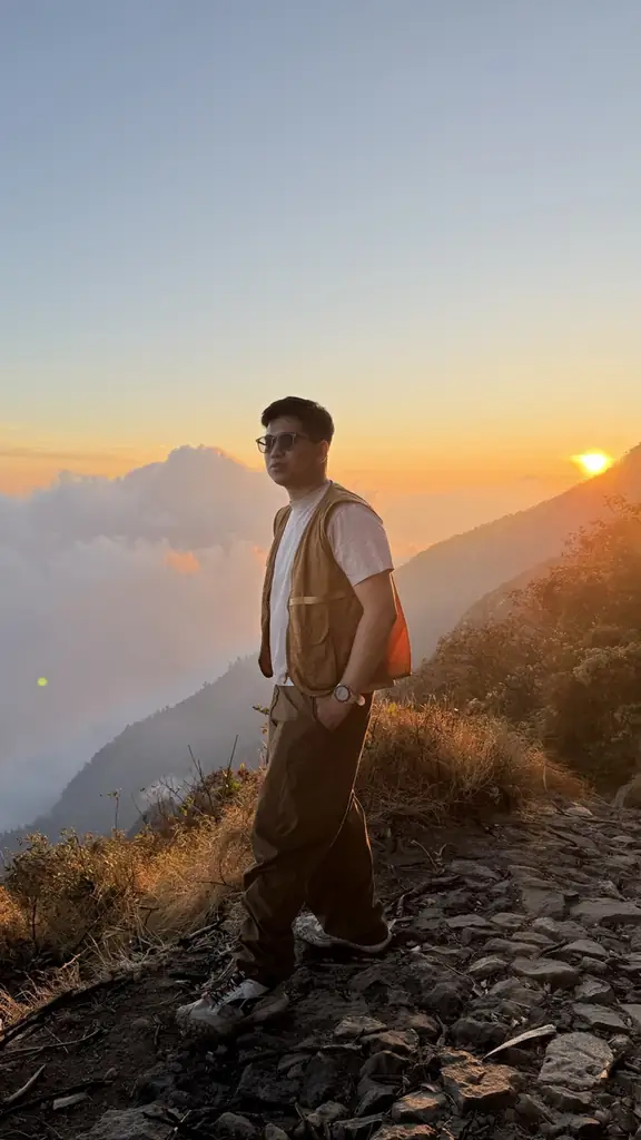 Gin berdiri di punggungan gunung pas matahari terbenam, di atas lautan awan.